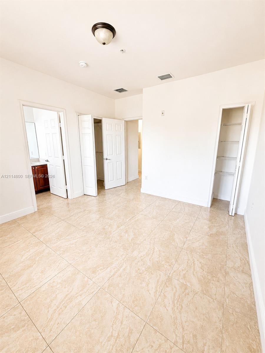 Room with tile flooring, two closets with bi-fold doors, a single-light dome ceiling fixture, and a white six-panel door