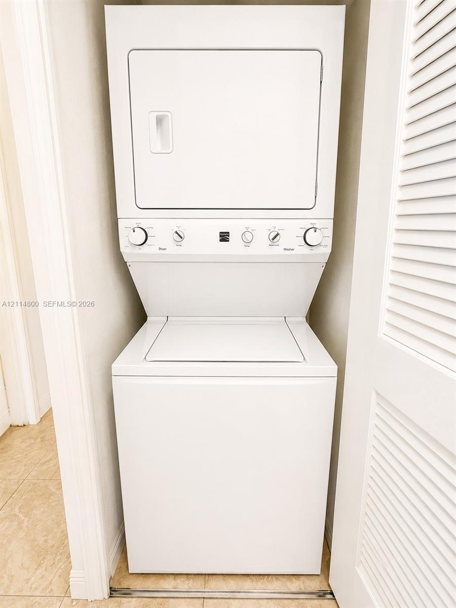 White stackable laundry unit enclosed within a closet featuring louvered doors