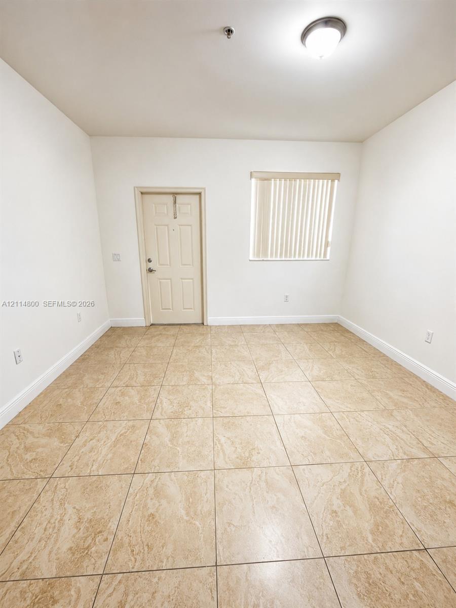 Interior space featuring neutral wall tones, large-format tile flooring, a window with vertical blinds, and a flush-mount ceiling light fixture