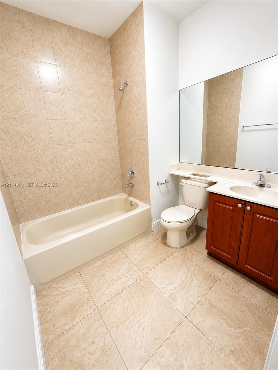 Bathroom featuring a tub-shower combination with floor-to-ceiling tile surround, large-format tile flooring, a wood-finish vanity with a solid-surface countertop, and a full-width wall-mounted mirror