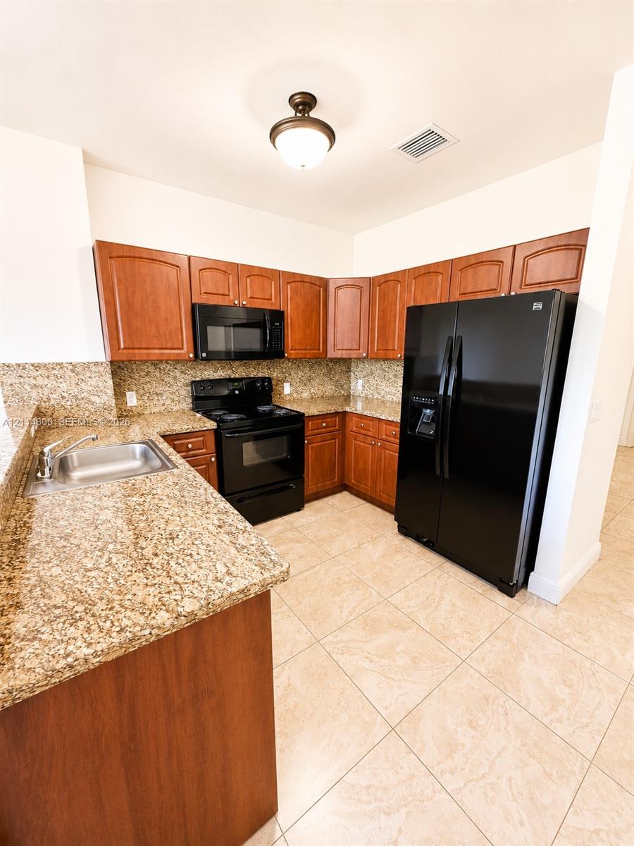 Kitchen featuring wood cabinetry, stone countertops, black appliances, tile flooring, and a drop-in stainless steel sink