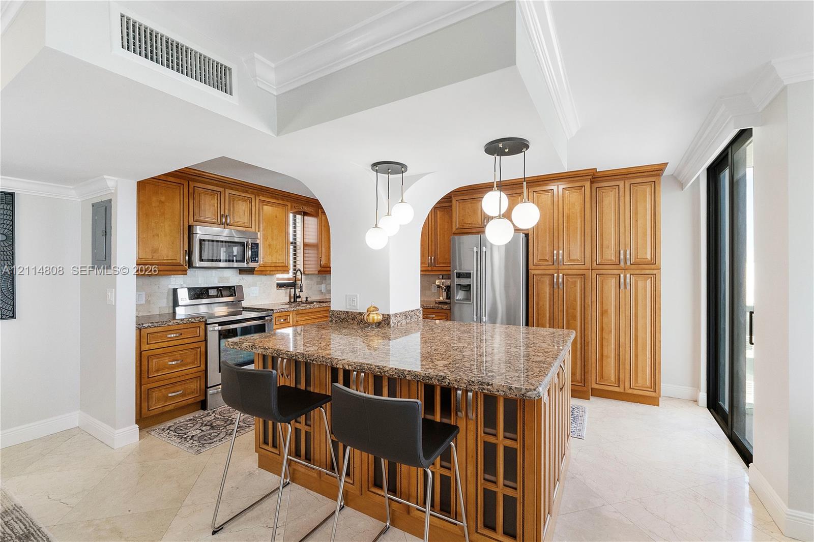 Kitchen featuring stone countertops, custom cabinetry, a center island, stainless steel appliances, and pendant lighting