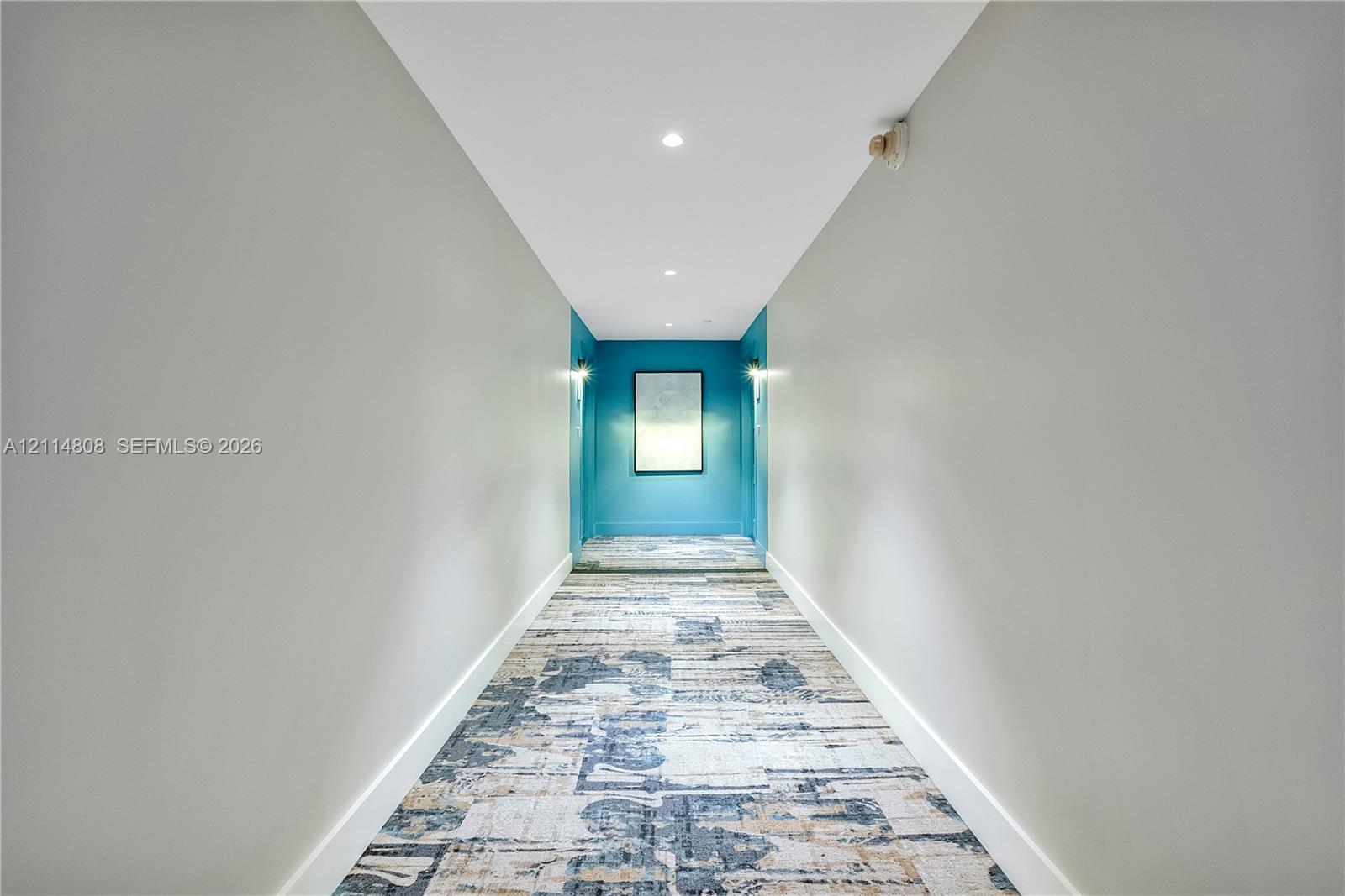 Hallway featuring neutral-toned walls, patterned textile floor covering, recessed ceiling lighting, and wall-mounted light fixtures