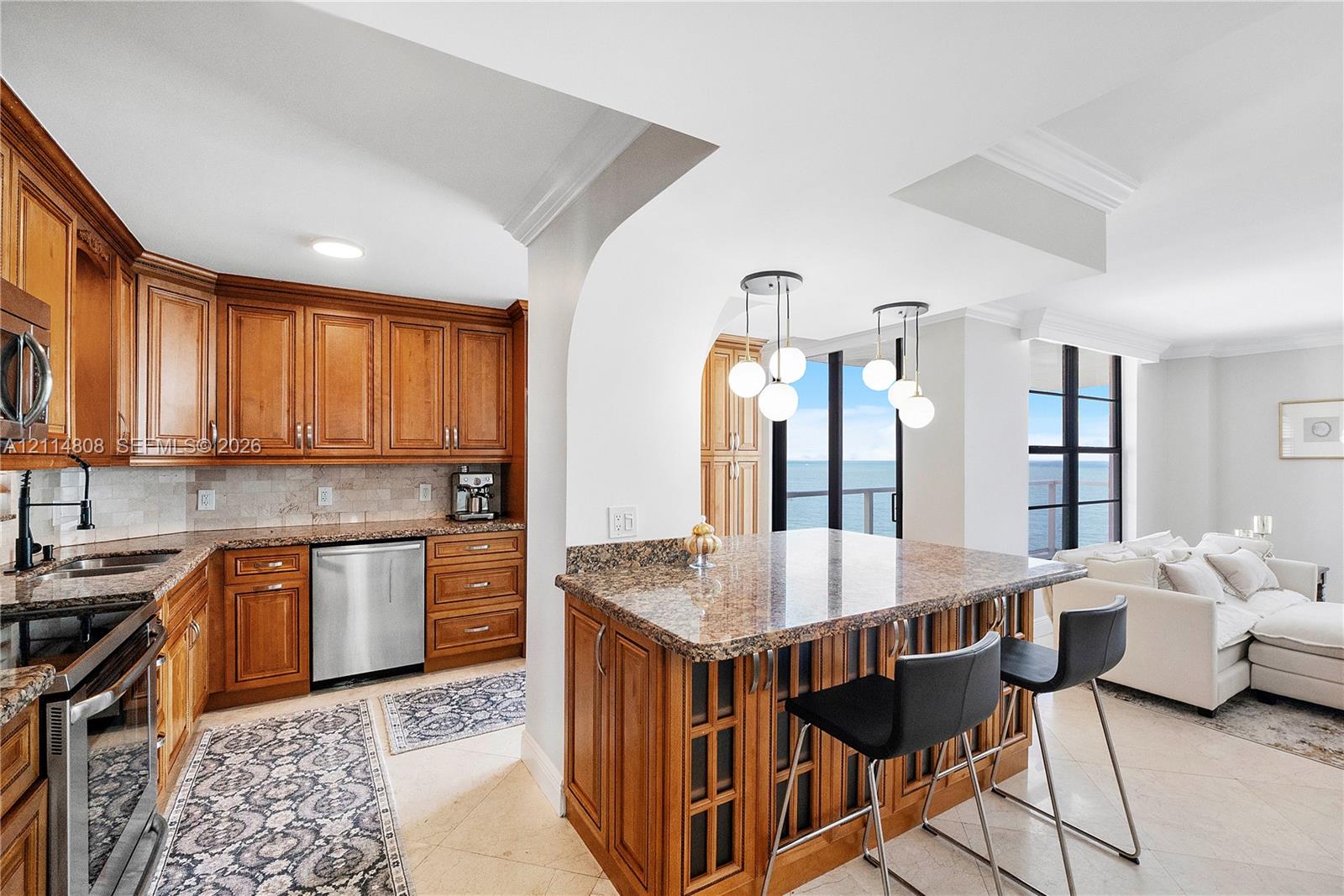 Kitchen featuring wood cabinetry, stone countertops, stone tile backsplash, stainless steel appliances, and multi-light pendant fixtures over a breakfast bar