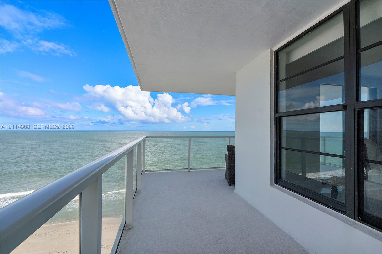 Private covered balcony featuring a glass panel railing, concrete flooring, and direct ocean exposure