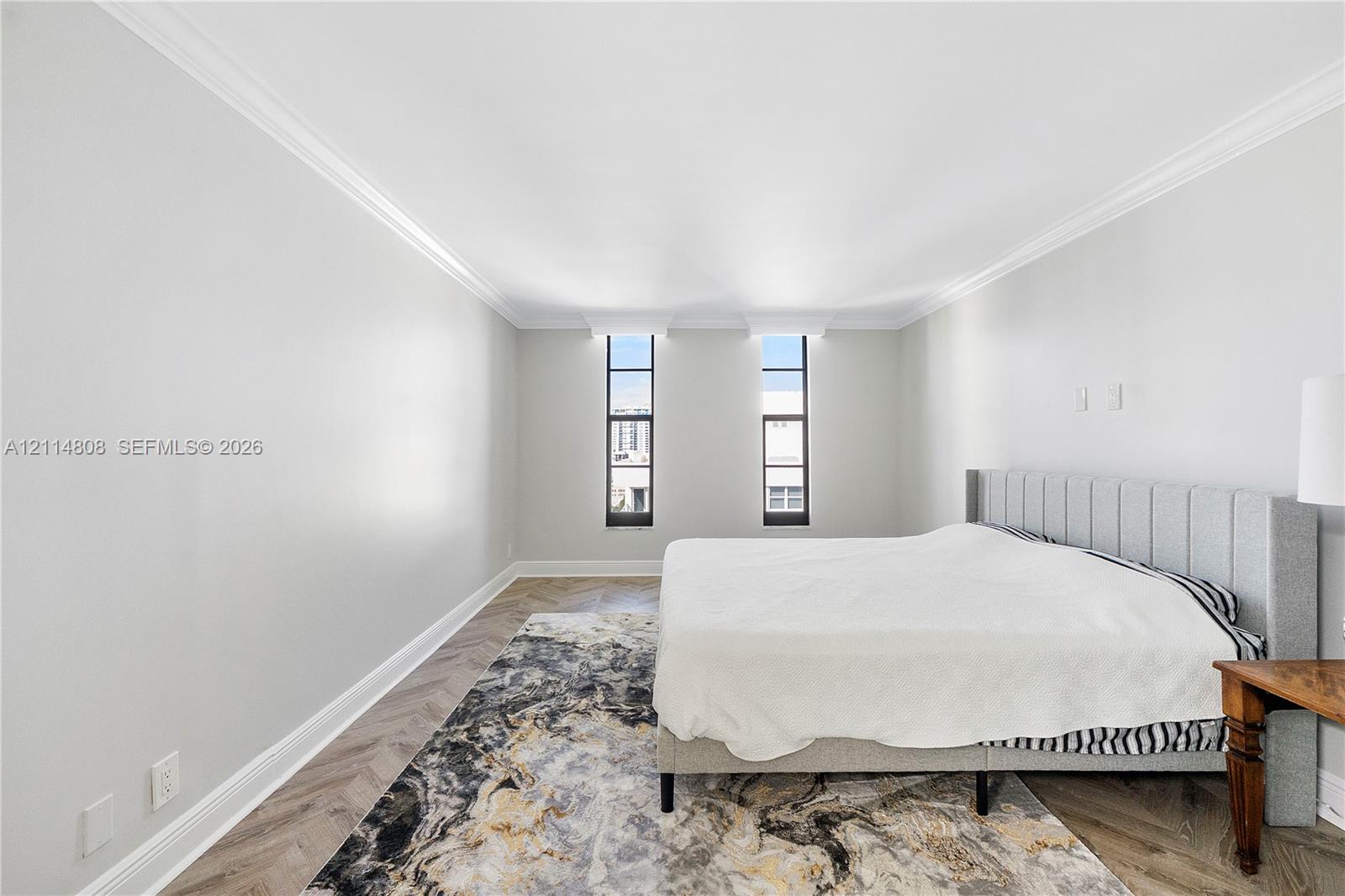Herringbone-patterned wood-finish flooring, neutral wall tones, crown molding, and dual tall windows