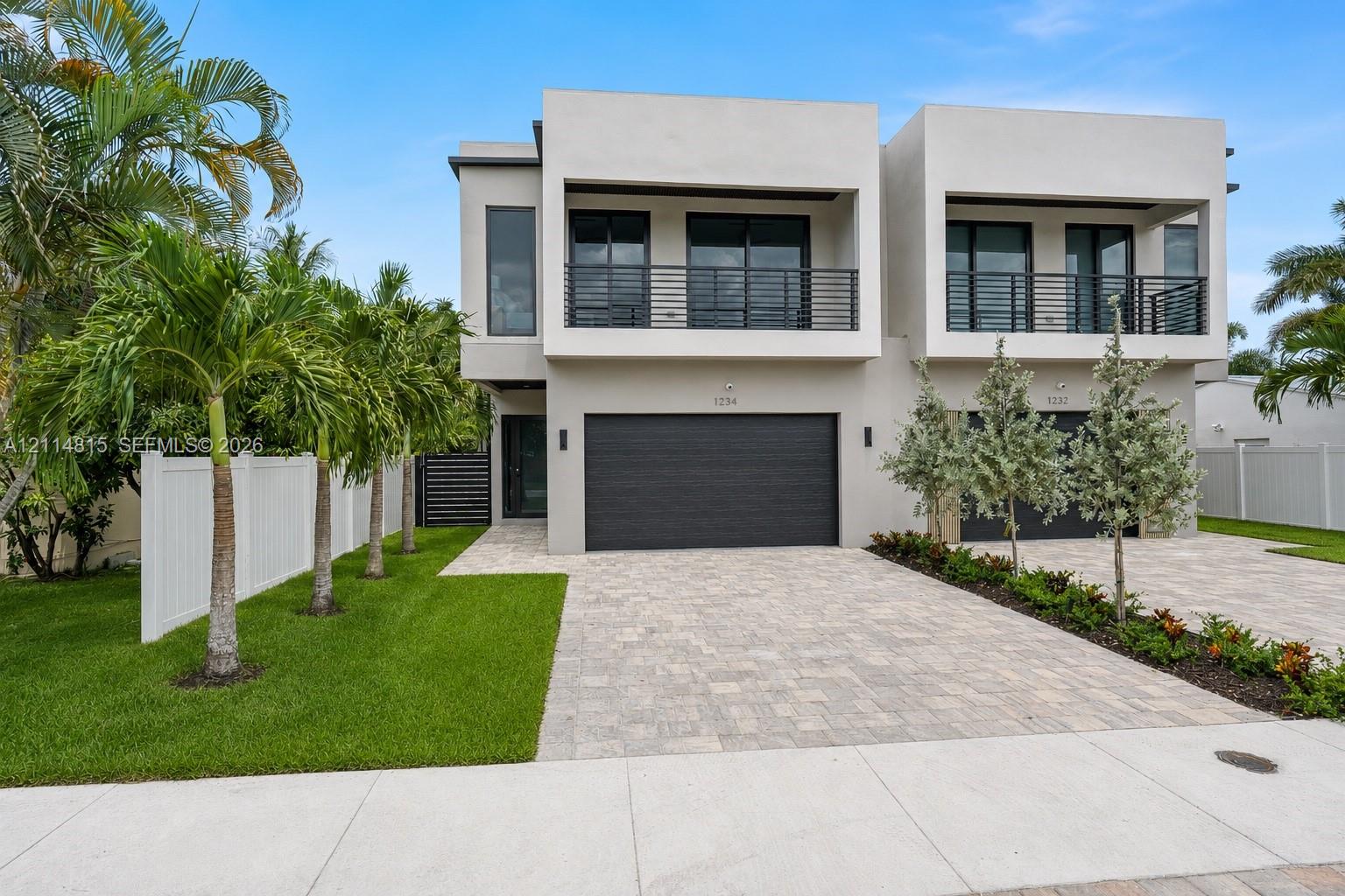 Modern architectural exterior featuring smooth stucco finish, paver driveway, dark-toned sectional garage doors, and second-story balconies with horizontal metal railings Modern architectural exterior featuring smooth stucco finish, paver driveway, dark-toned sectional garage doors, and second-story balconies with horizontal metal railings