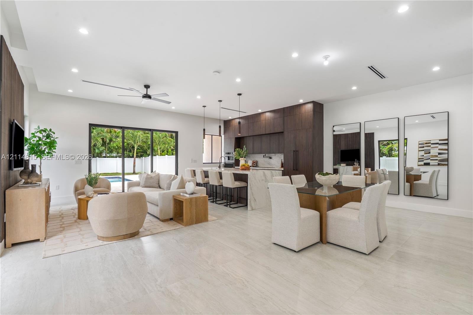 Open-concept interior featuring large-format tile flooring, recessed ceiling lighting, a kitchen island with waterfall-edge countertop, dark-toned cabinetry, and floor-to-ceiling sliding glass doors Open-concept interior featuring large-format tile flooring, recessed ceiling lighting, a kitchen island with waterfall-edge countertop, dark-toned cabinetry, and floor-to-ceiling sliding glass doors