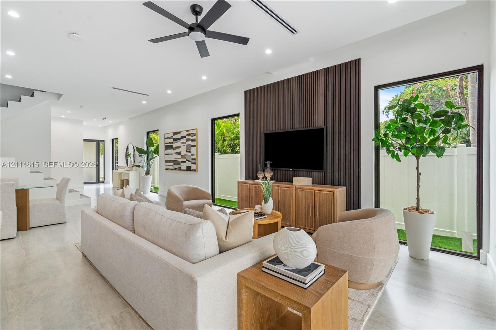 Open-concept space featuring large-format tile flooring, a floor-to-ceiling dark wood-slat accent wall, recessed lighting, a modern ceiling fan, and expansive glass doors Open-concept space featuring large-format tile flooring, a floor-to-ceiling dark wood-slat accent wall, recessed lighting, a modern ceiling fan, and expansive glass doors