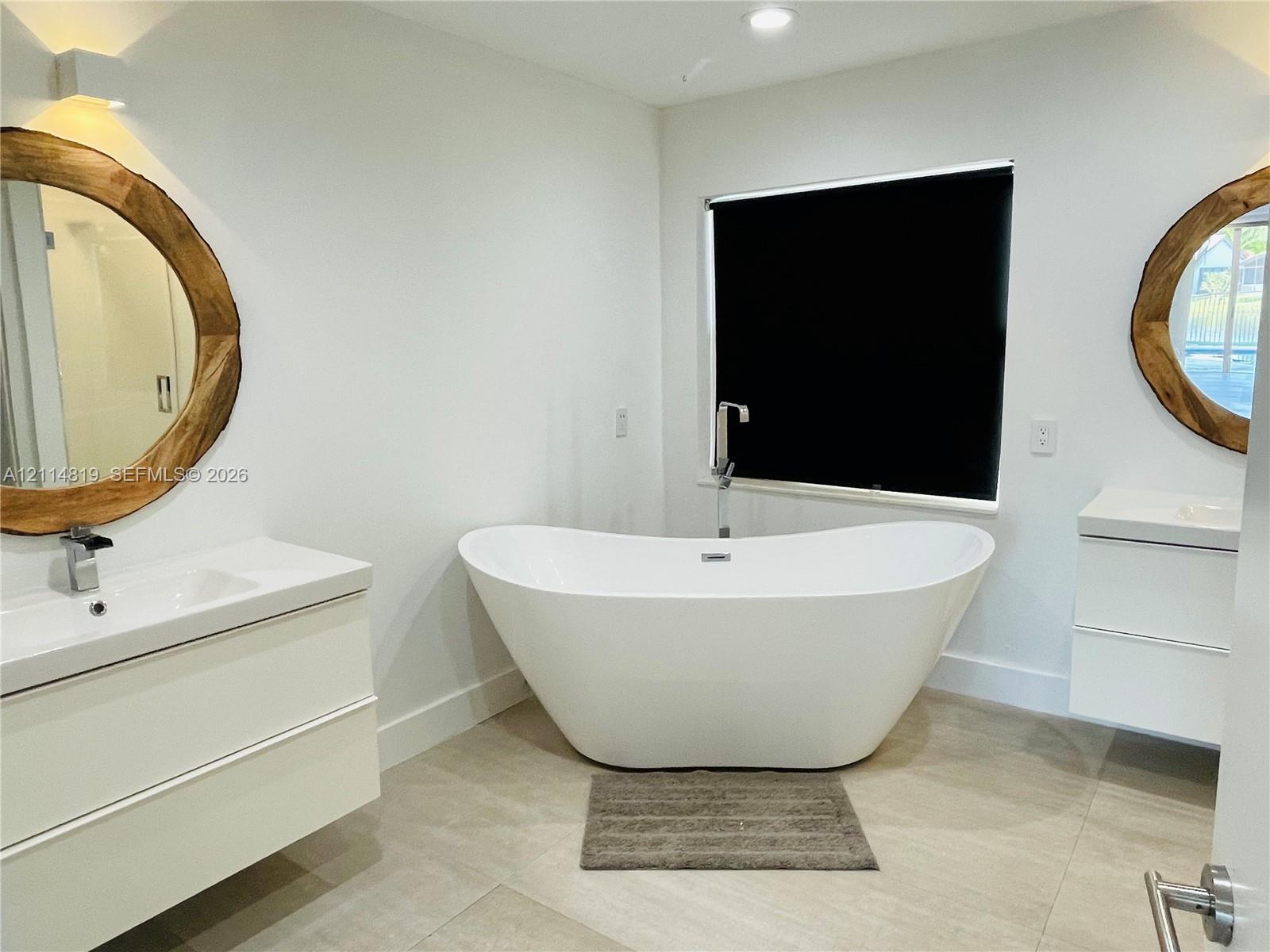 Freestanding soaking tub with chrome floor-mounted faucet, dual wall-mounted floating vanities with integrated rectangular sinks, and large-format tile flooring
