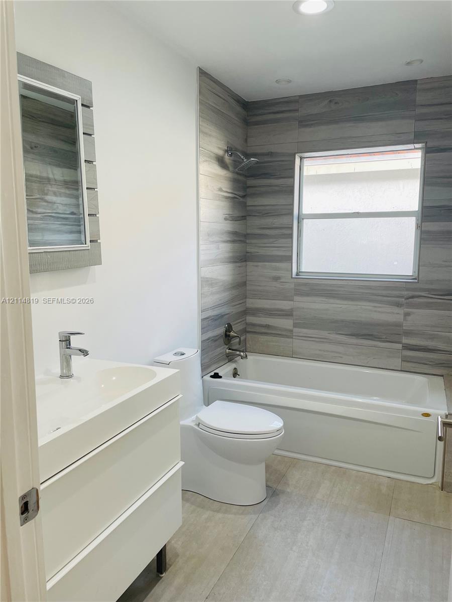 Modern bathroom featuring a white floating vanity with a vessel sink, dual-flush toilet, built-in bathtub with a shower fixture, and grey-toned tile surround