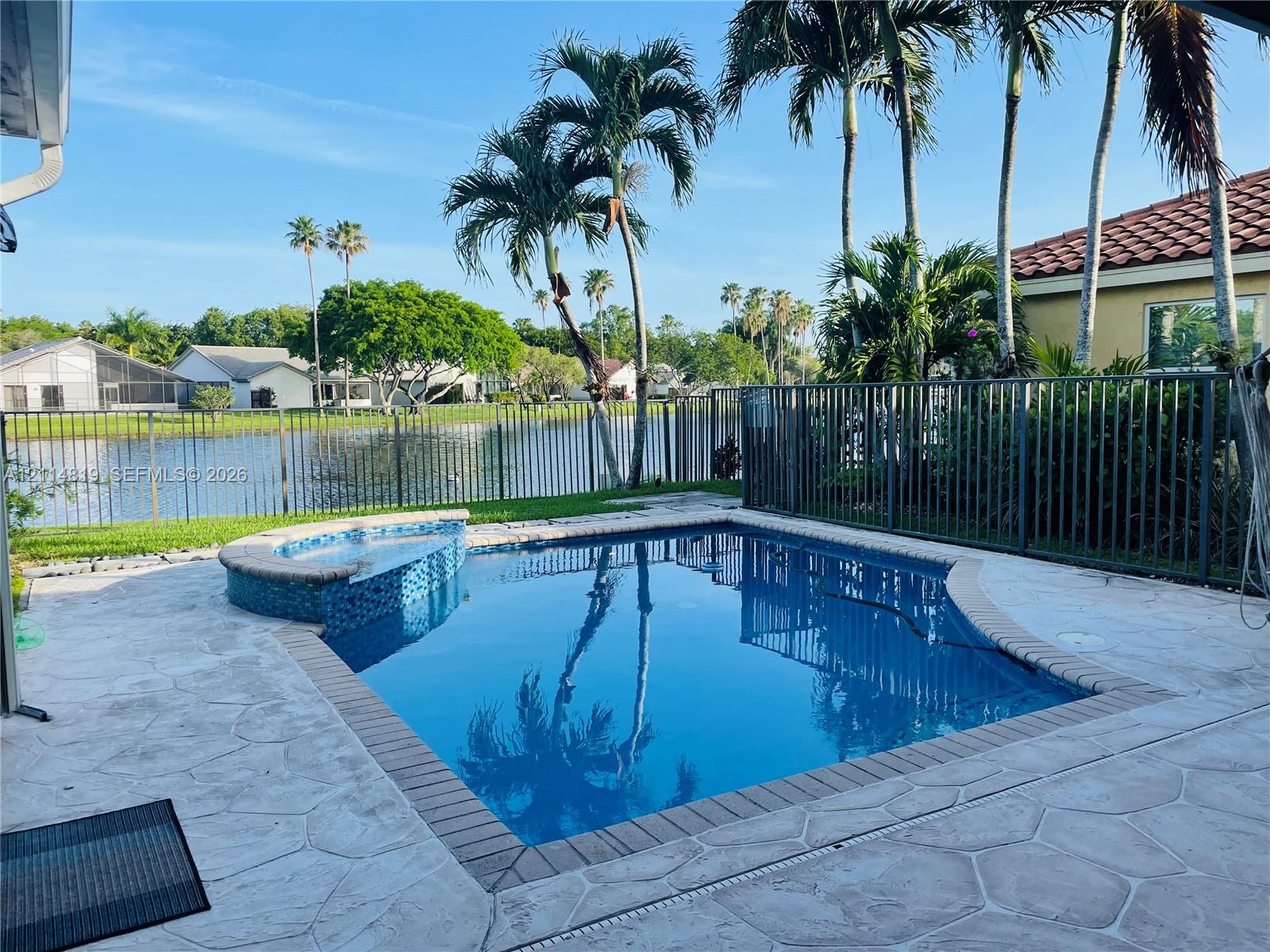Backyard pool with a raised spillover spa, stamped concrete decking, and metal perimeter fencing overlooking a pond