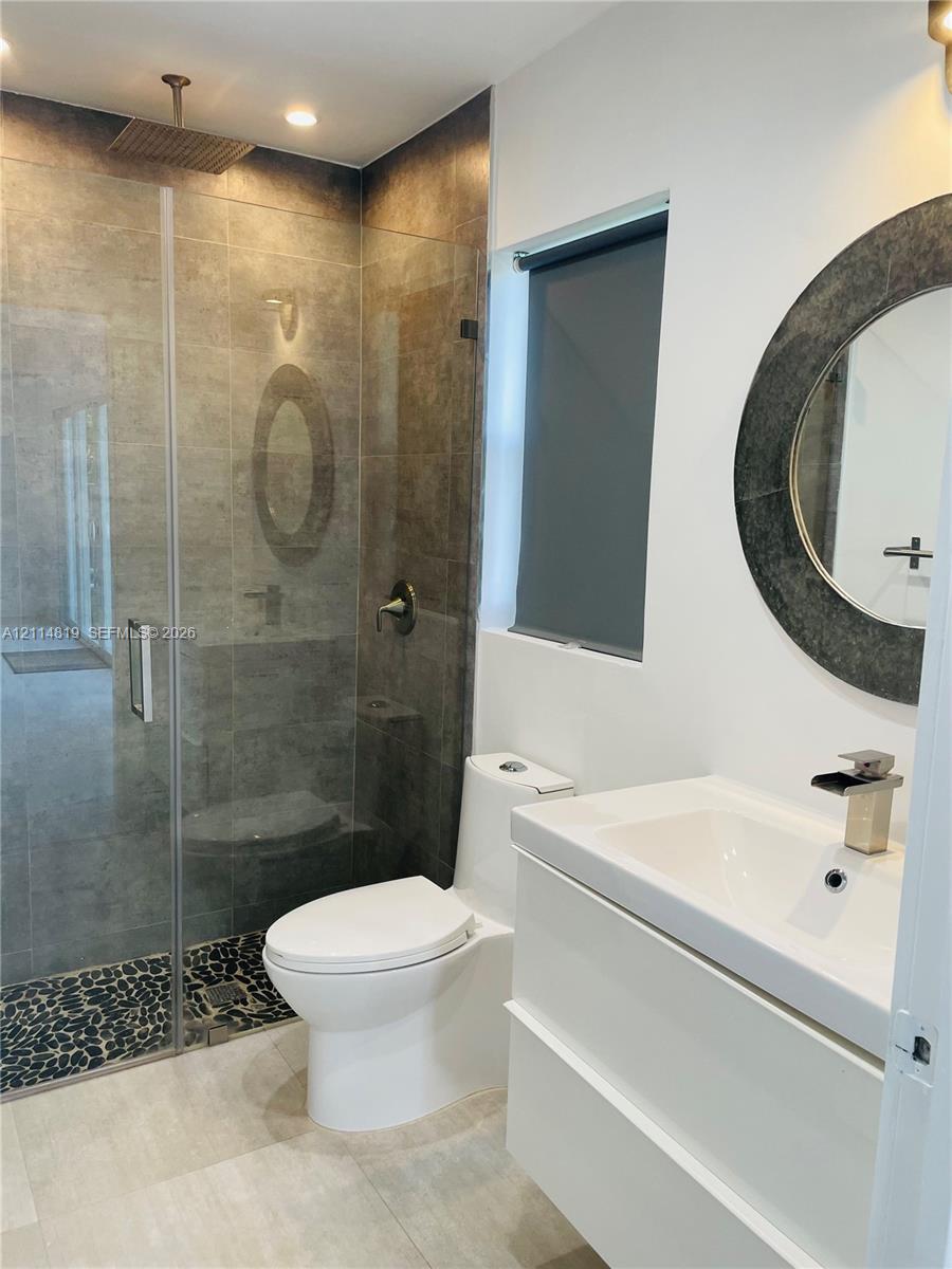 Modern bathroom featuring a glass-enclosed shower with a rainfall showerhead, pebble-stone flooring, a white floating vanity, and a circular wall mirror