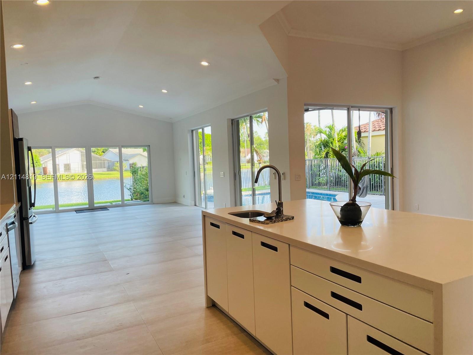 Open-concept kitchen featuring an island with a solid-surface countertop and undermount sink, recessed ceiling lighting, light-toned flooring, and wall-to-wall sliding glass doors