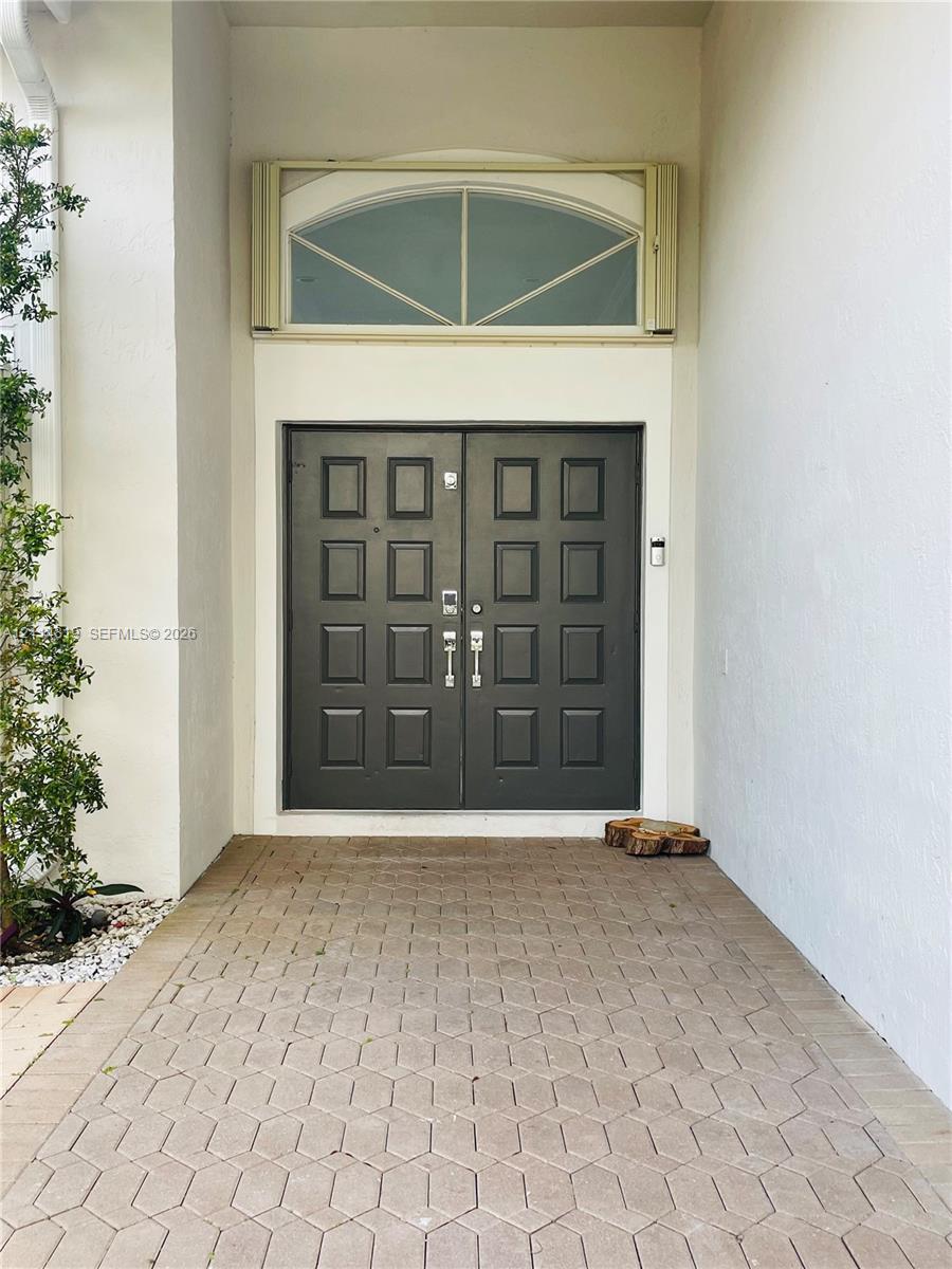 Covered entryway featuring a paver stone porch, double entry doors with a paneled design, and a stationary arched transom window