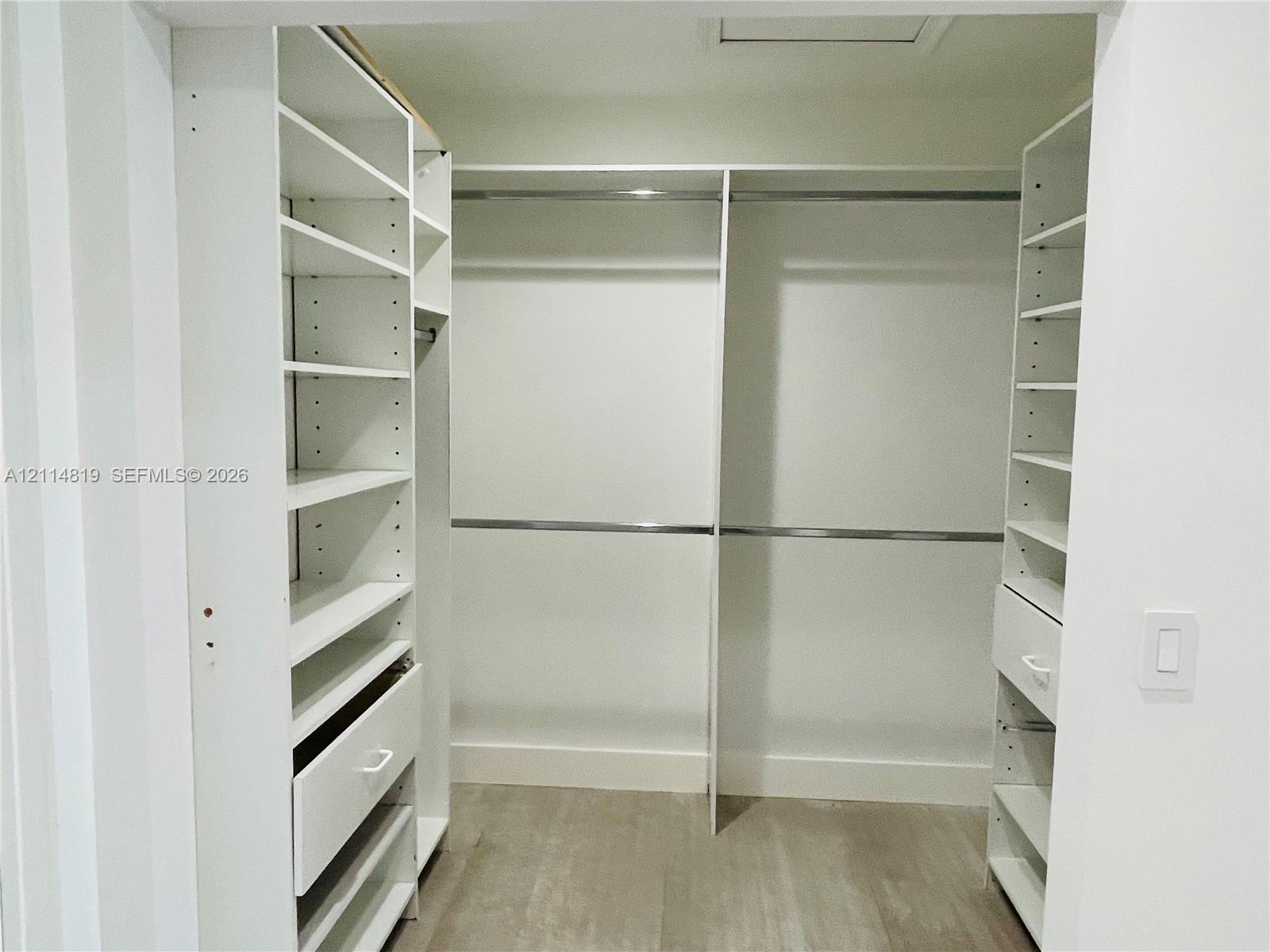 Walk-in closet featuring white built-in shelving, integrated drawers, metal hanging rods, and wood-finish flooring