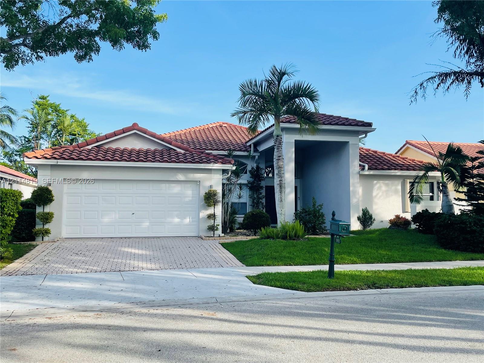 Stucco exterior featuring a multi-gabled tile roof, paver driveway, attached two-car garage, and manicured landscaping