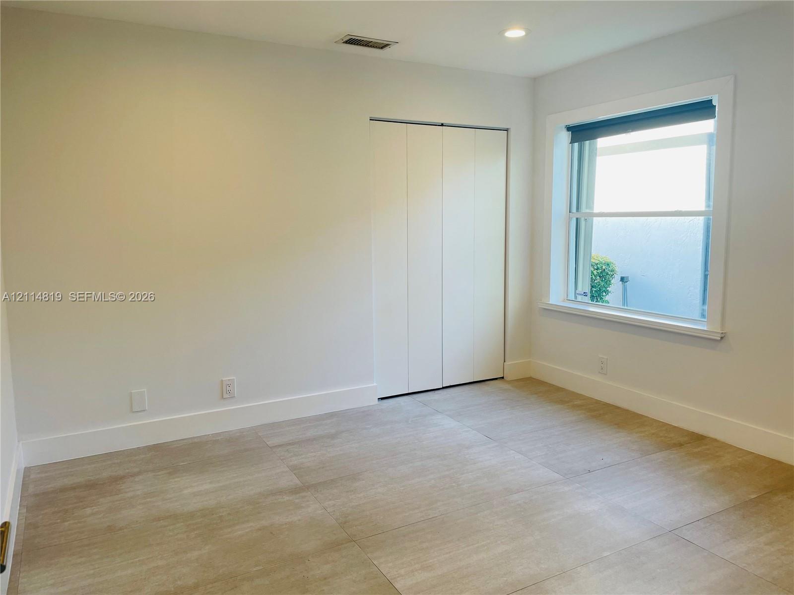 Neutral-toned interior room featuring large-format tile flooring, recessed ceiling lighting, a single-pane window, and a built-in folding closet door