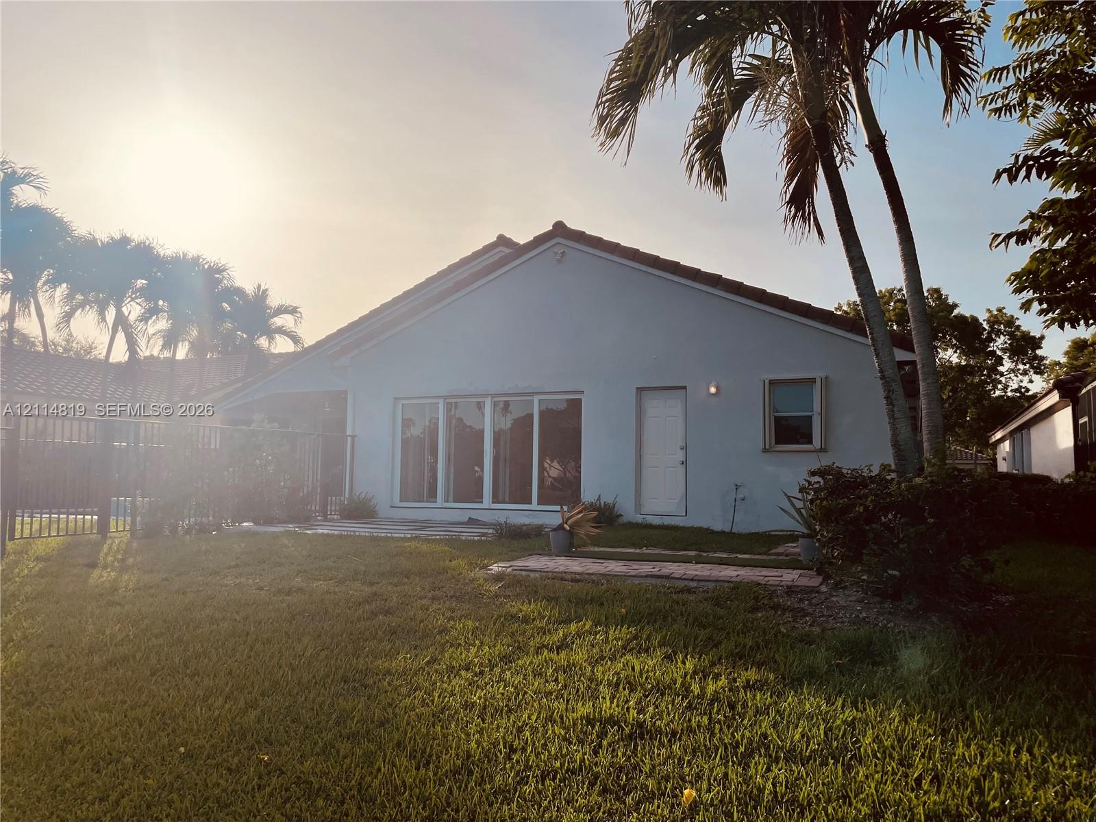 Stucco exterior featuring a tiled roof, large glass sliding doors, a paved patio area, and mature palm trees
