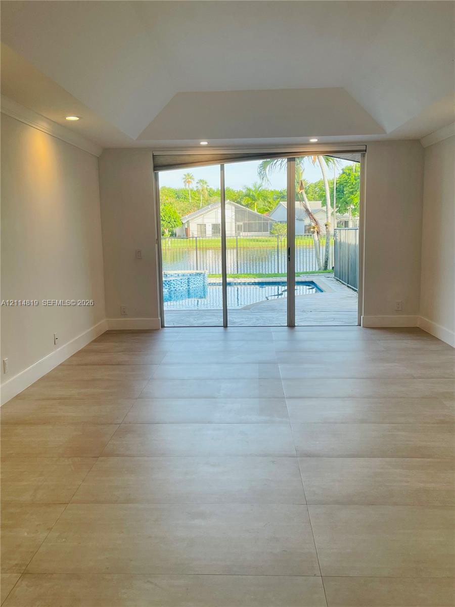 Tray ceiling with recessed lighting, large-format tile flooring, and floor-to-ceiling sliding glass doors opening to a swimming pool and water frontage