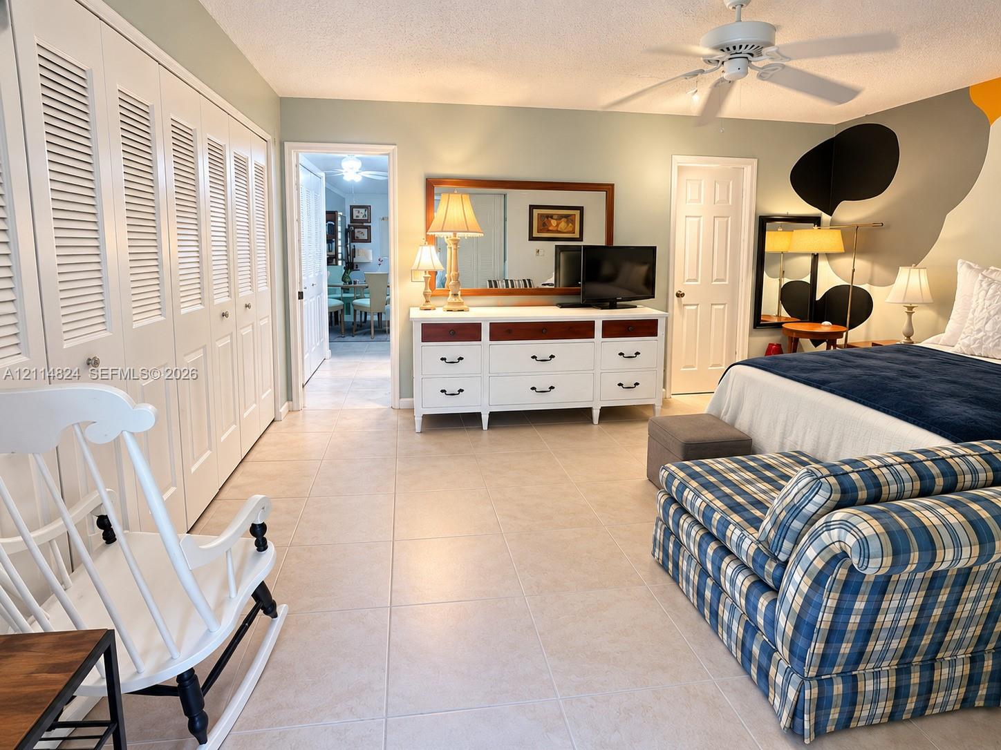 Large room featuring neutral tile flooring, louvered closet doors, and a ceiling fan with integrated lighting