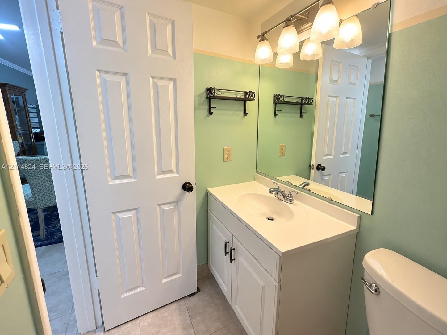White vanity featuring an integrated sink, polished chrome faucet, matte black hardware, and an expansive wall-mounted mirror with multi-bulb overhead lighting