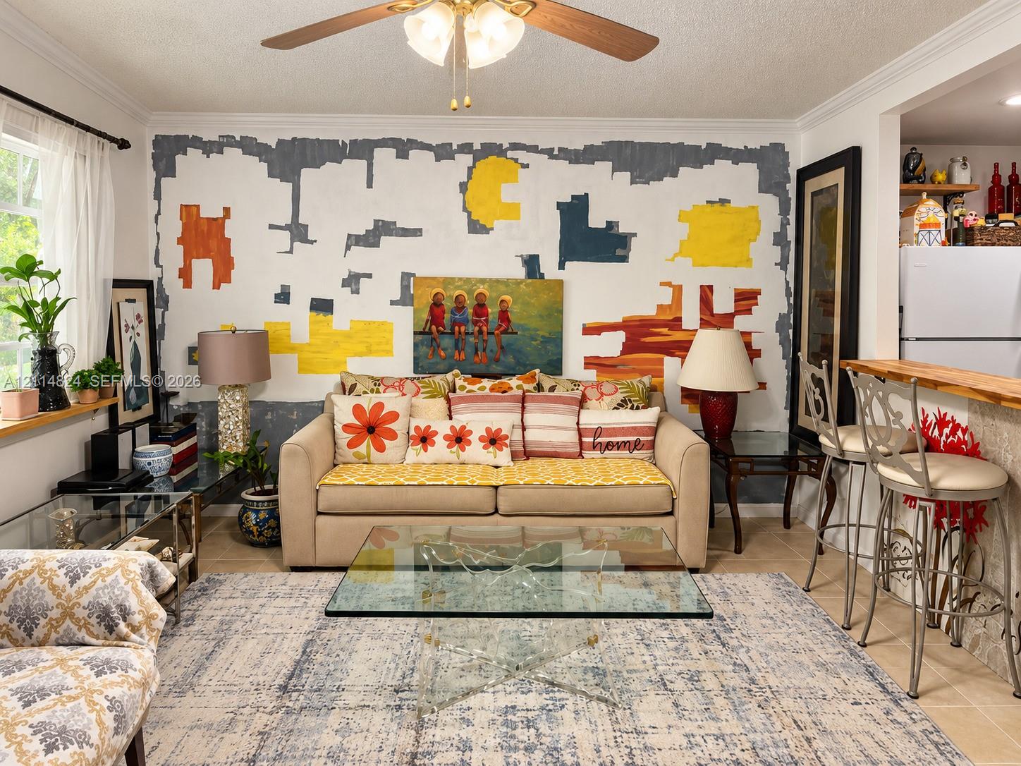 Neutral tile flooring, breakfast bar with a wood-finish countertop, and a ceiling-mounted light fixture with a fan