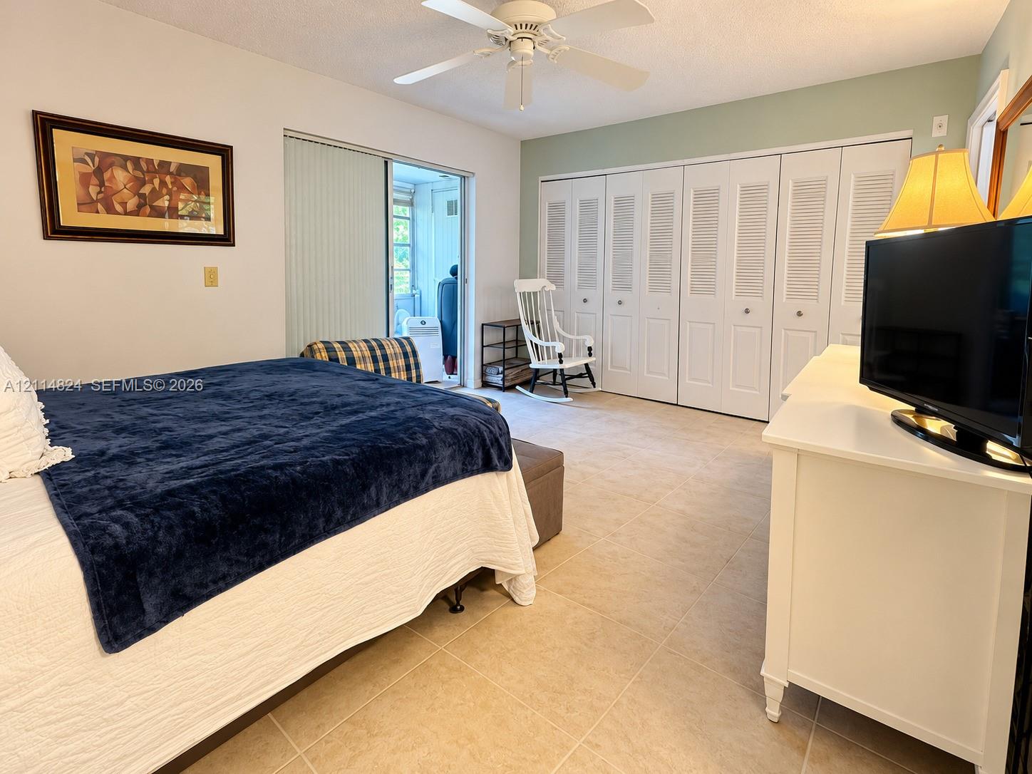 Bedroom featuring tile flooring, sliding glass patio doors, a ceiling fan with integrated lighting, and multiple louvered-style closet doors