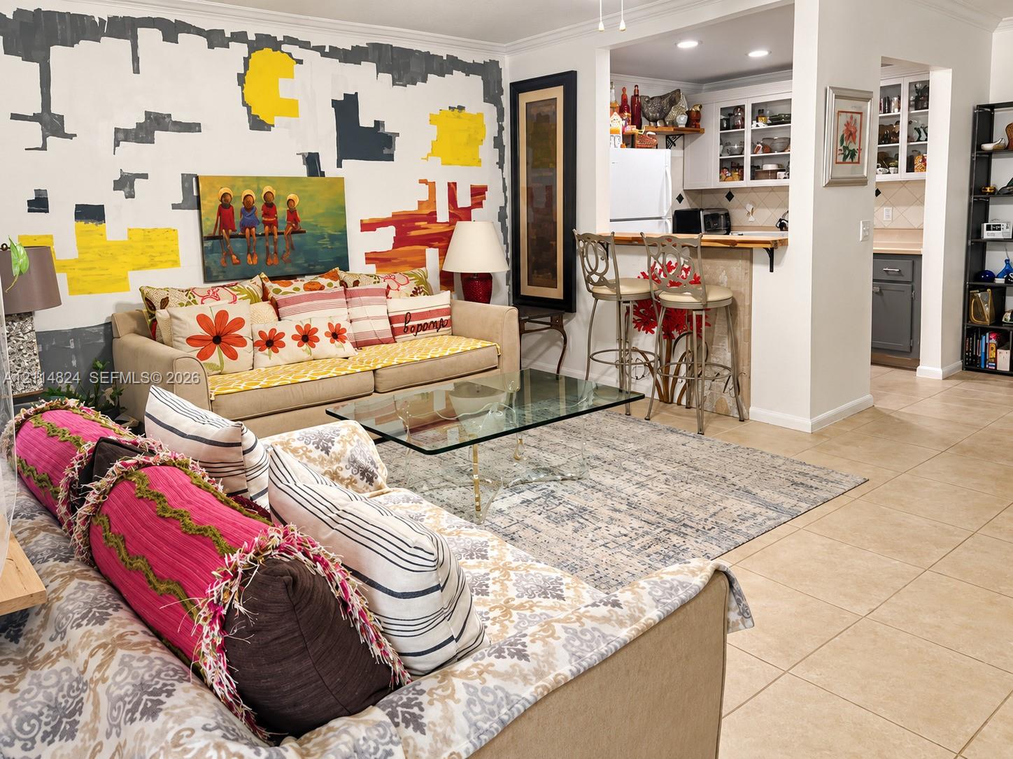 Open-concept interior featuring light-toned tile flooring, built-in kitchen cabinetry with integrated glass-front display storage, and a pass-through breakfast bar with a tile-faced counter
