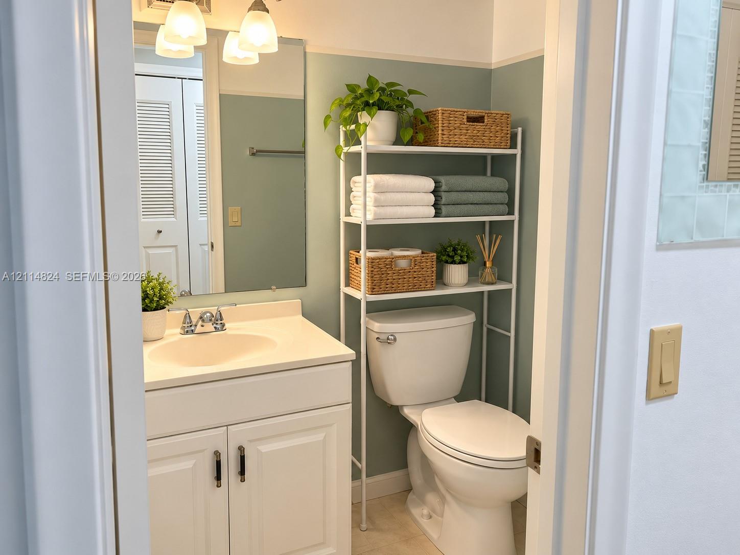 Bathroom featuring a white vanity cabinet, integrated countertop basin, three-light wall-mounted fixture, and louvered-style closet doors