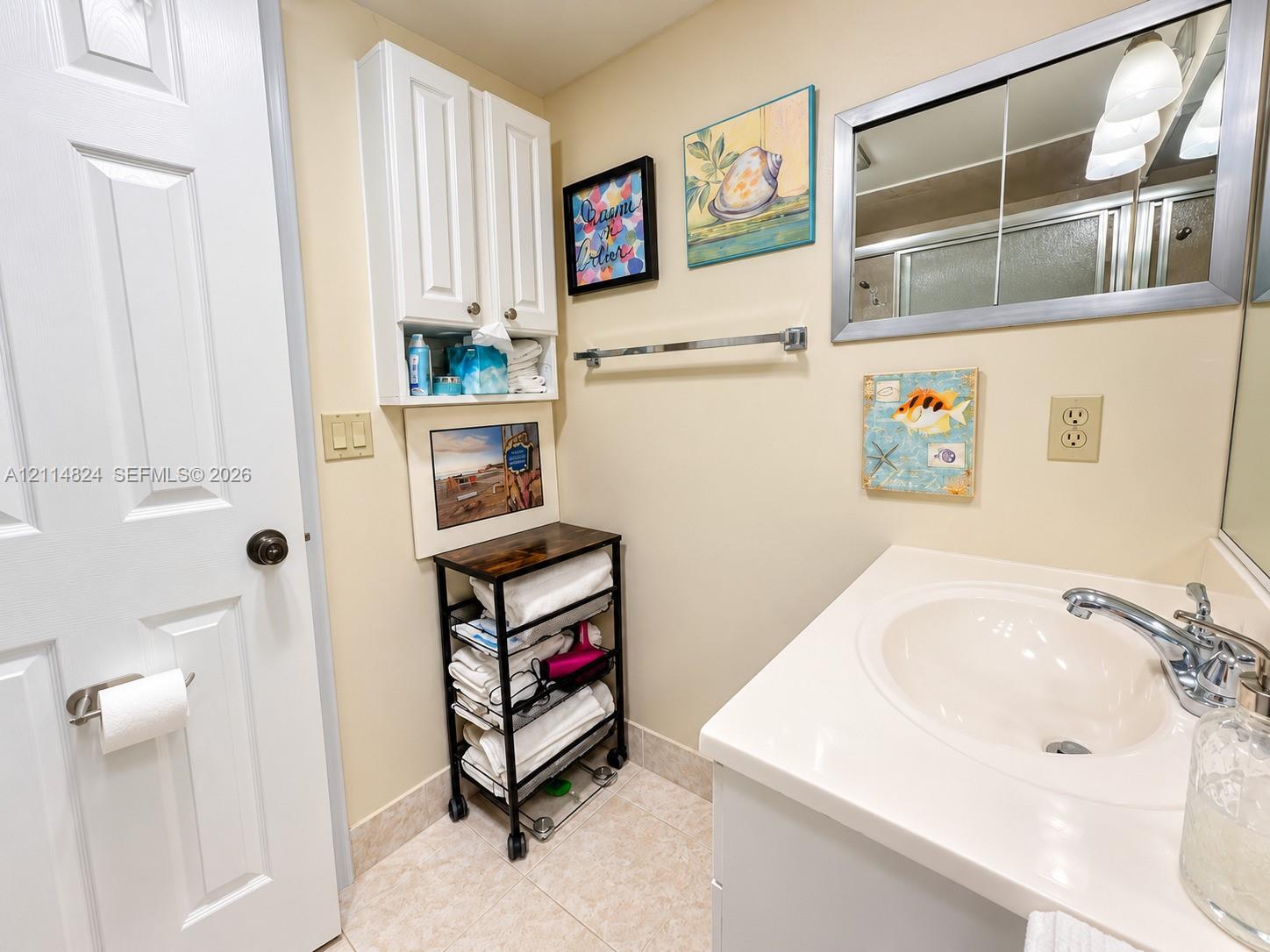 Bathroom vanity featuring a white cabinet base, integrated sink with a chrome-finished faucet, wall-mounted medicine cabinet with a mirrored front, and additional upper storage cabinetry