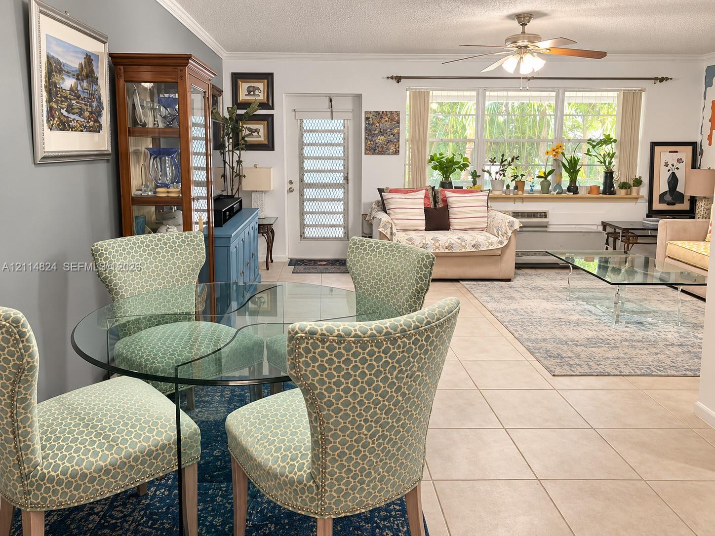 Living area featuring large format tile flooring, crown molding, a central ceiling fan, and extensive windows