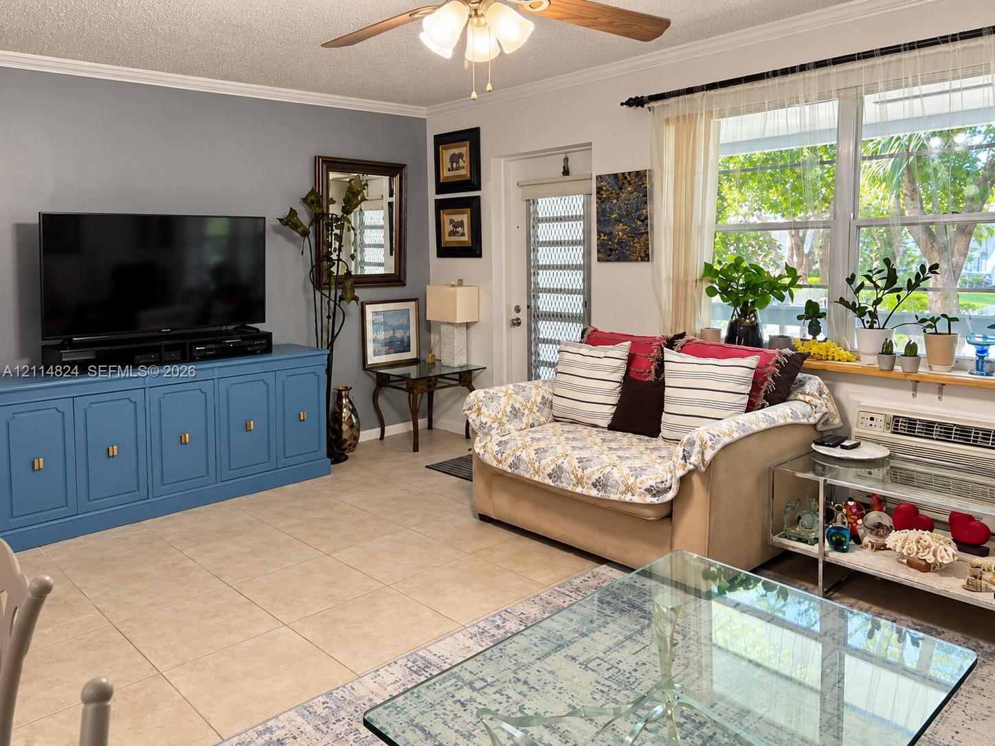 Living area featuring large-format tile flooring, built-in blue storage cabinetry, ceiling fan with integrated lighting, and a metal security door