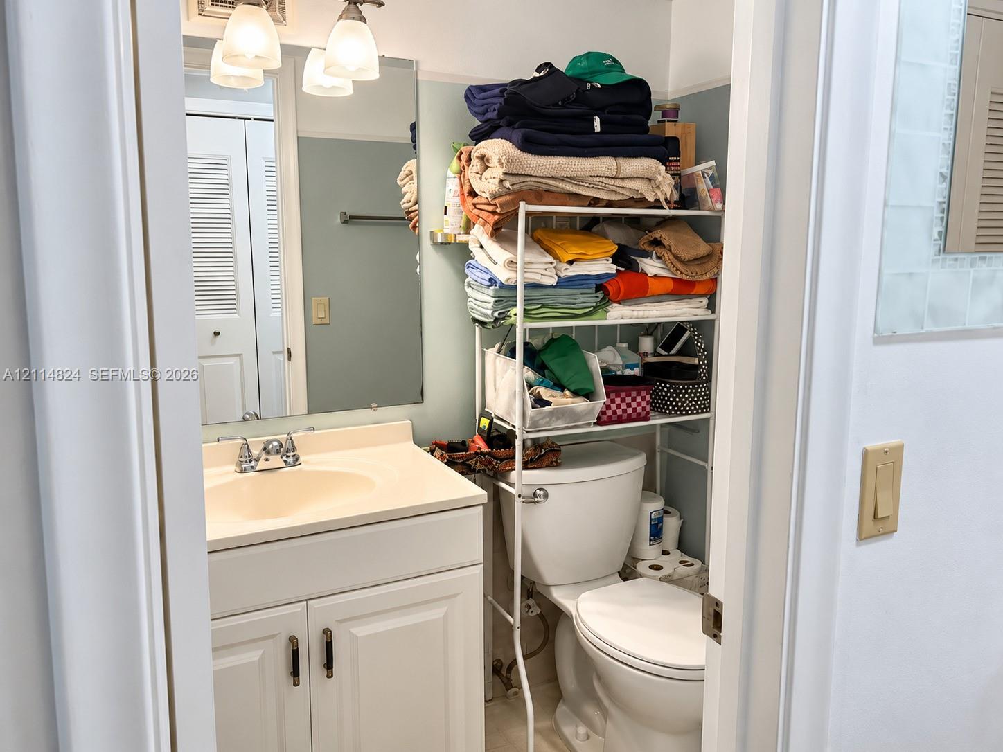 Bathroom featuring a vanity with an integrated sink and basin, white shaker-style cabinetry, and a wall-mounted mirror with integrated three-bulb lighting fixture