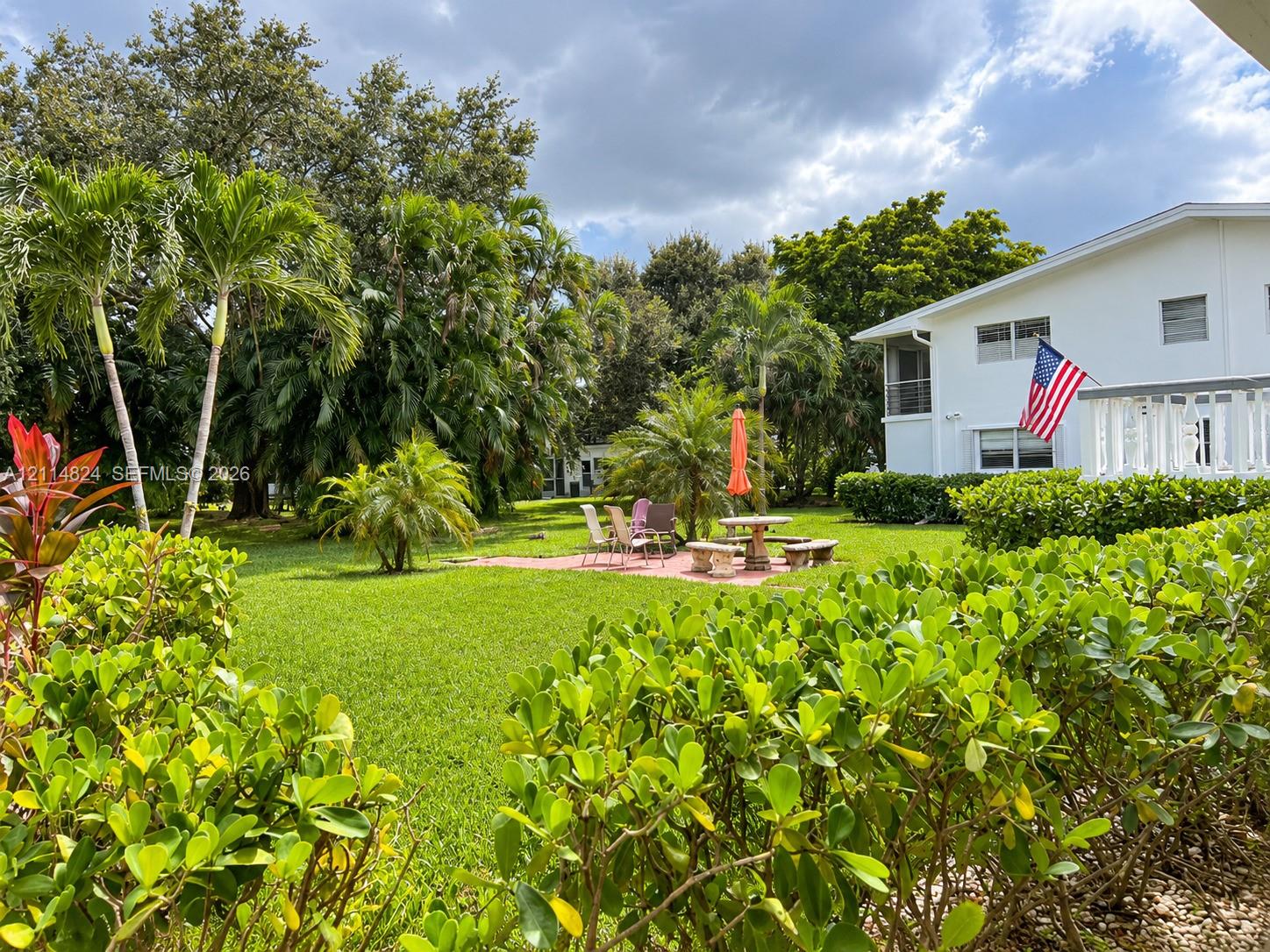 Expansive grounds featuring a manicured lawn, established palm trees, a brick paver patio, and low-maintenance perimeter shrubbery