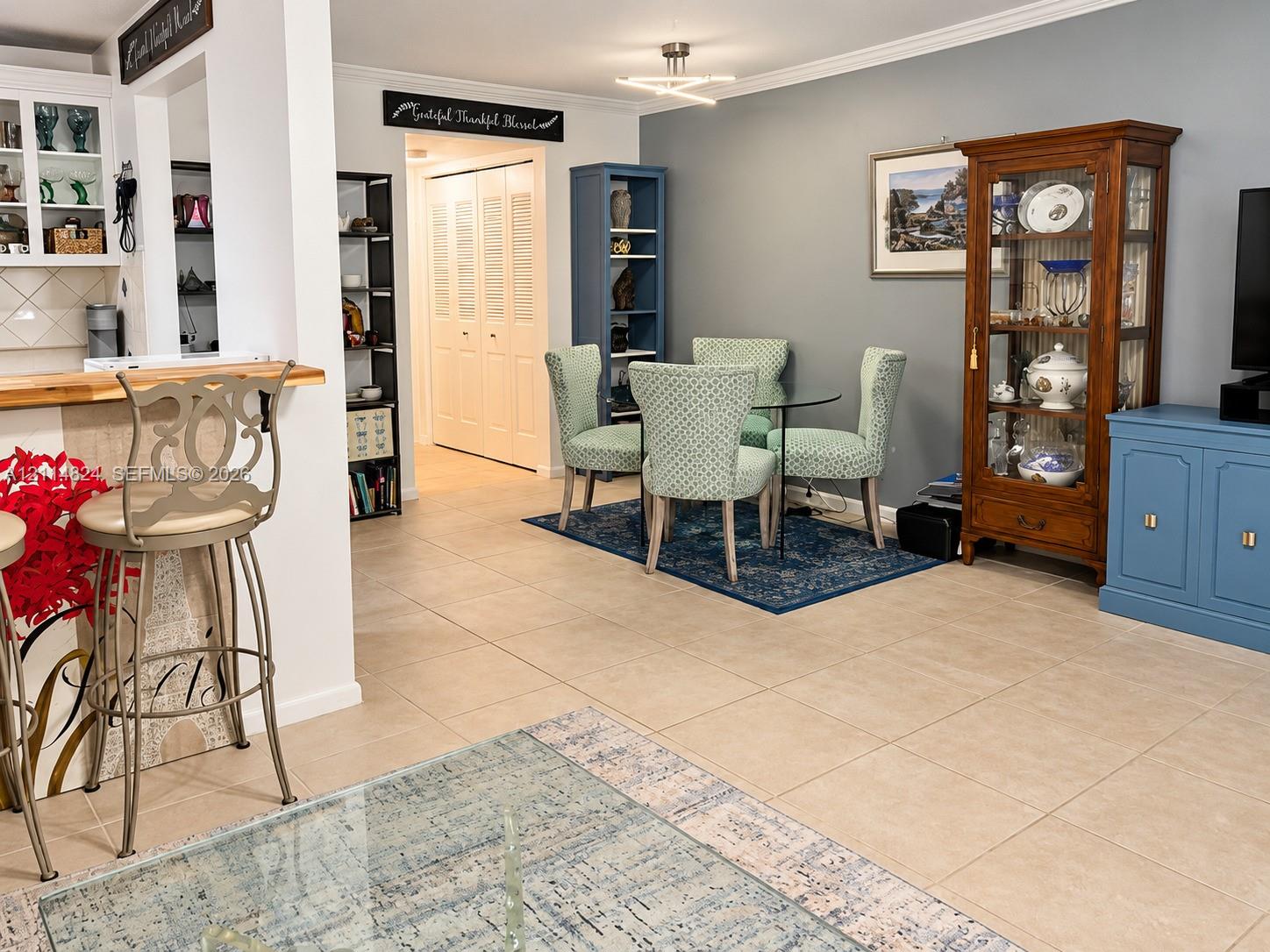 Neutral-toned tile flooring, built-in breakfast bar with a wood-finish countertop, recessed shelving, and a modern geometric ceiling light fixture