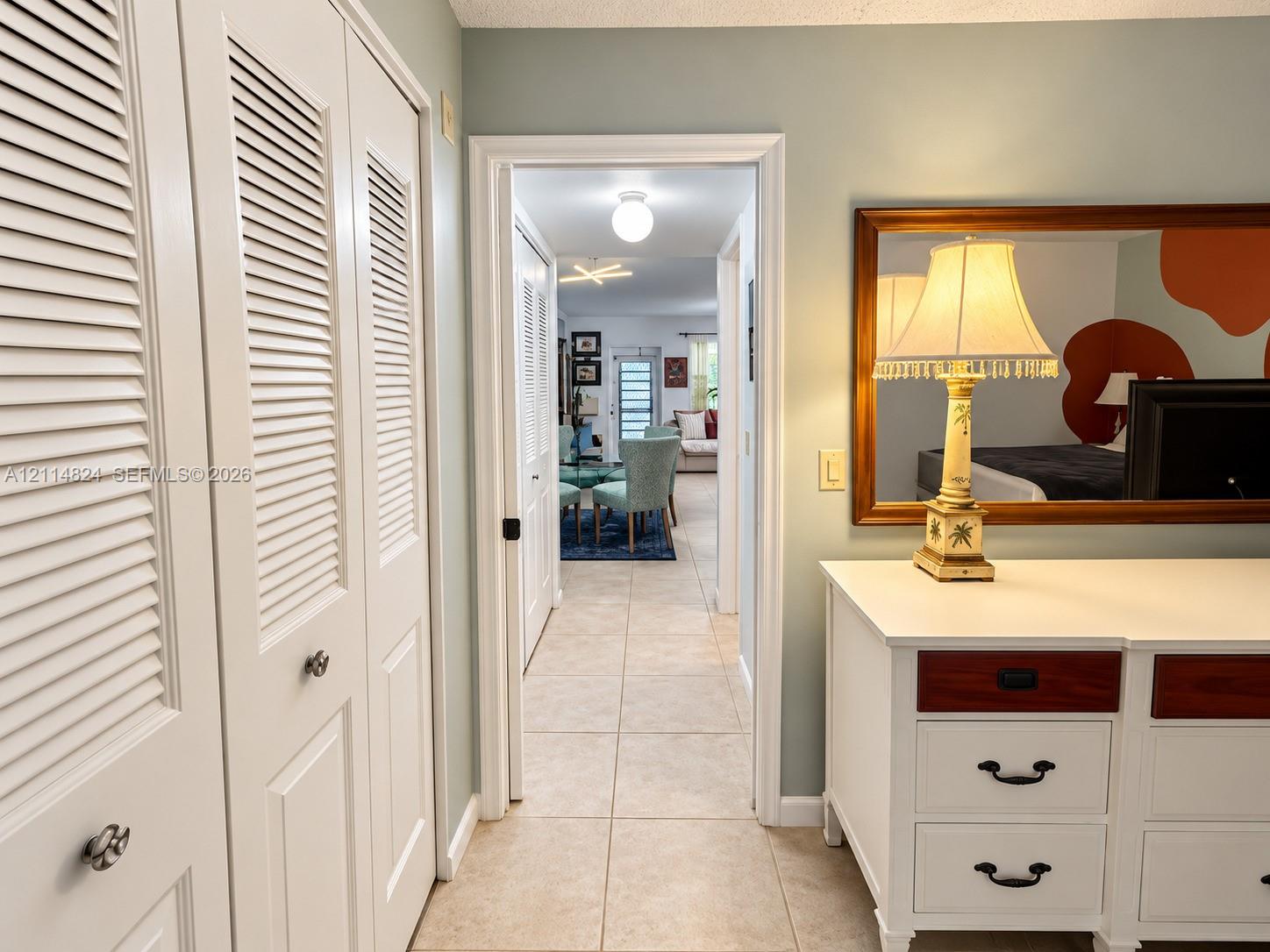 Hallway featuring neutral-toned floor tile and white louvered-panel closets