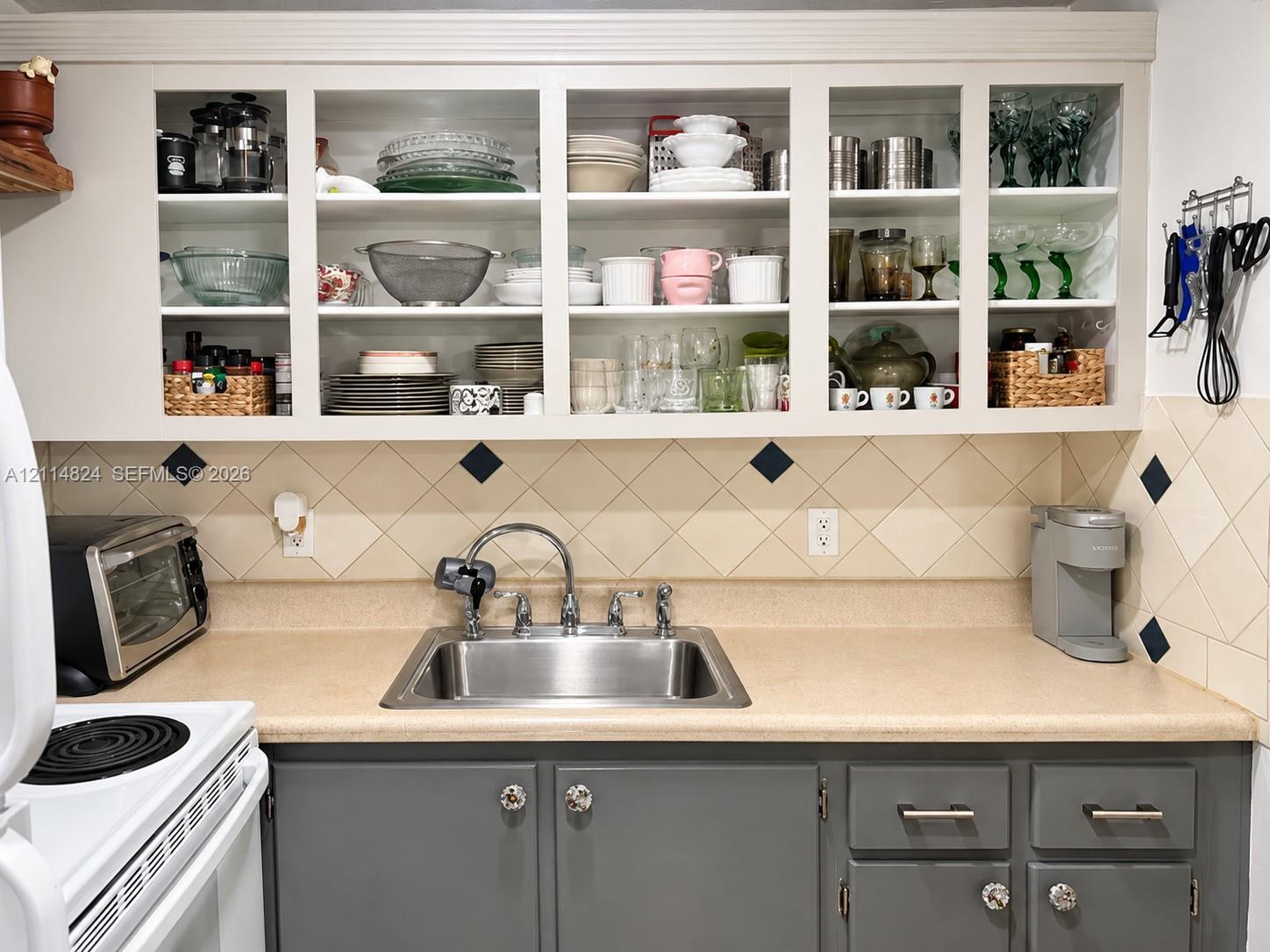 Kitchen featuring grey lower cabinetry with metallic hardware, solid-surface countertops, a stainless steel undermount sink, and glass-front upper cabinets with integrated shelving