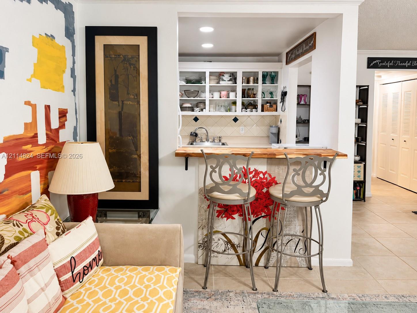 Kitchen pass-through featuring a wood-topped breakfast bar, white cabinetry with glass-panel doors, tile backsplash, recessed lighting, and a built-in sink