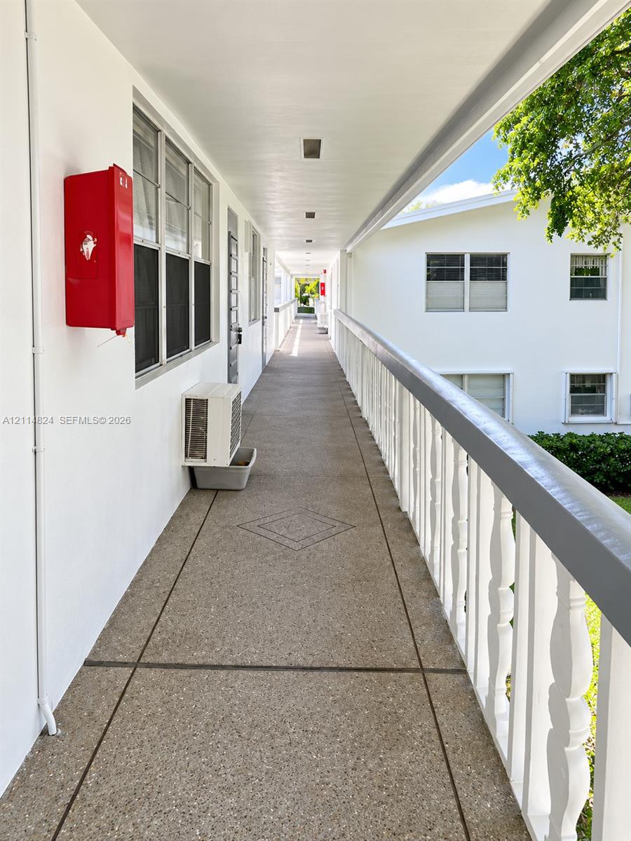 Covered exterior walkway featuring exposed aggregate flooring, geometric tile inlay, and a solid balustrade railing