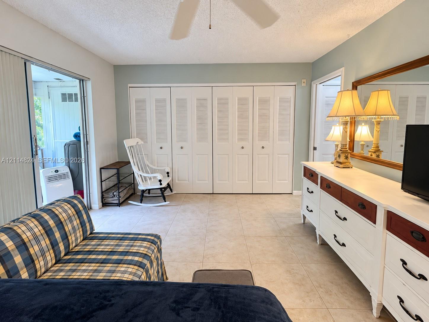 Neutral ceramic tile flooring, floor-to-ceiling louvered closet doors, and sliding glass patio door