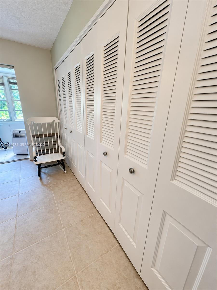 Extensive floor-to-ceiling storage featuring white louvered bifold doors with metallic hardware and neutral-tone ceramic tile flooring
