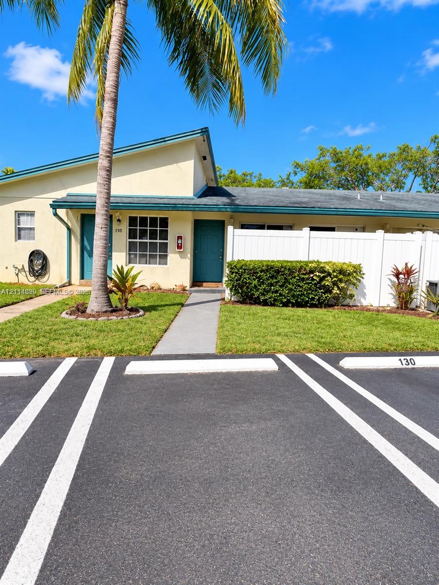 Exterior facade featuring a single-story design, dual entry doors, private white vinyl fencing, concrete walkways, and designated asphalt parking