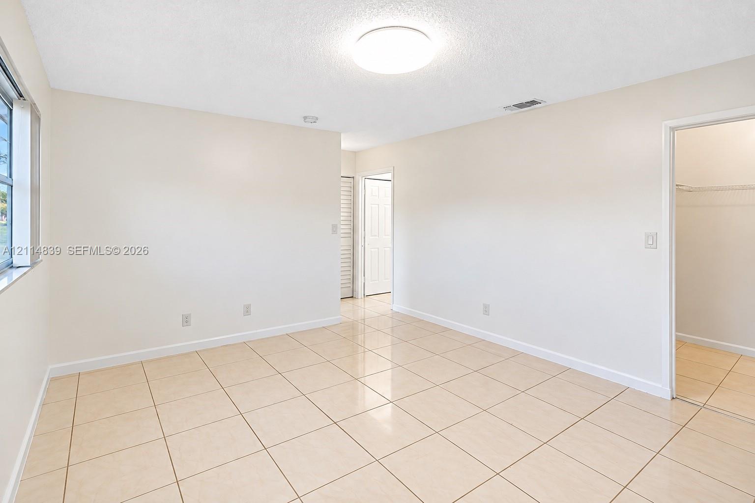 Neutral interior featuring large-format tile flooring, textured ceiling, flush-mount lighting, and a walk-in closet