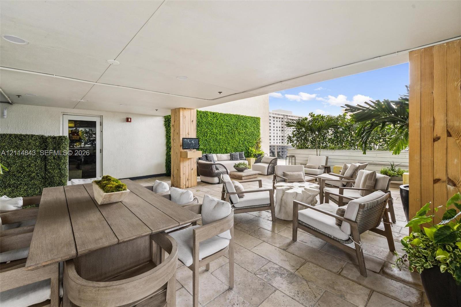 Covered outdoor terrace featuring stone tile flooring, structural columns with wood-finish cladding, and integrated artificial greenery wall accents
