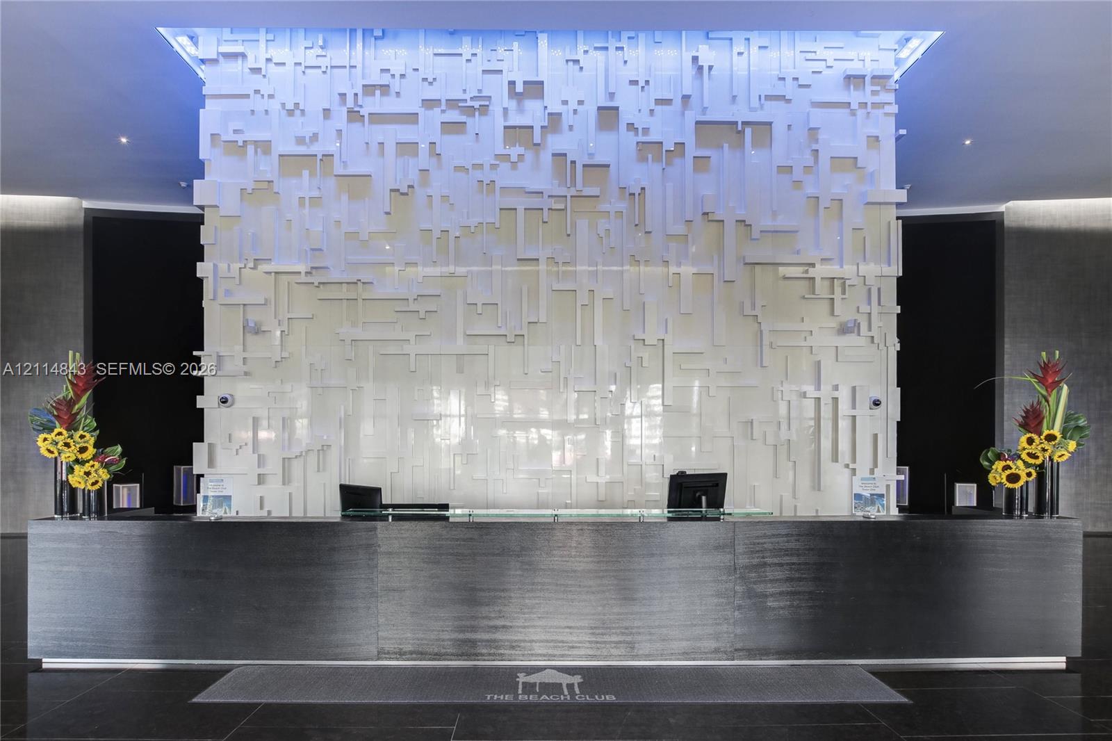 Lobby reception area featuring a high-contrast design, large-scale black service desk, three-dimensional textured accent wall, recessed cove lighting, and large-format dark stone flooring