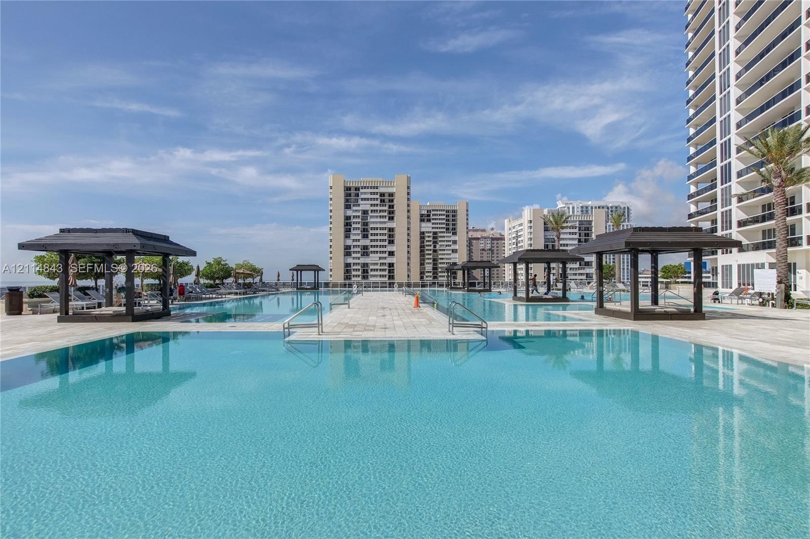 Expansive swimming pool with stone-tiled decking and multiple covered cabanas