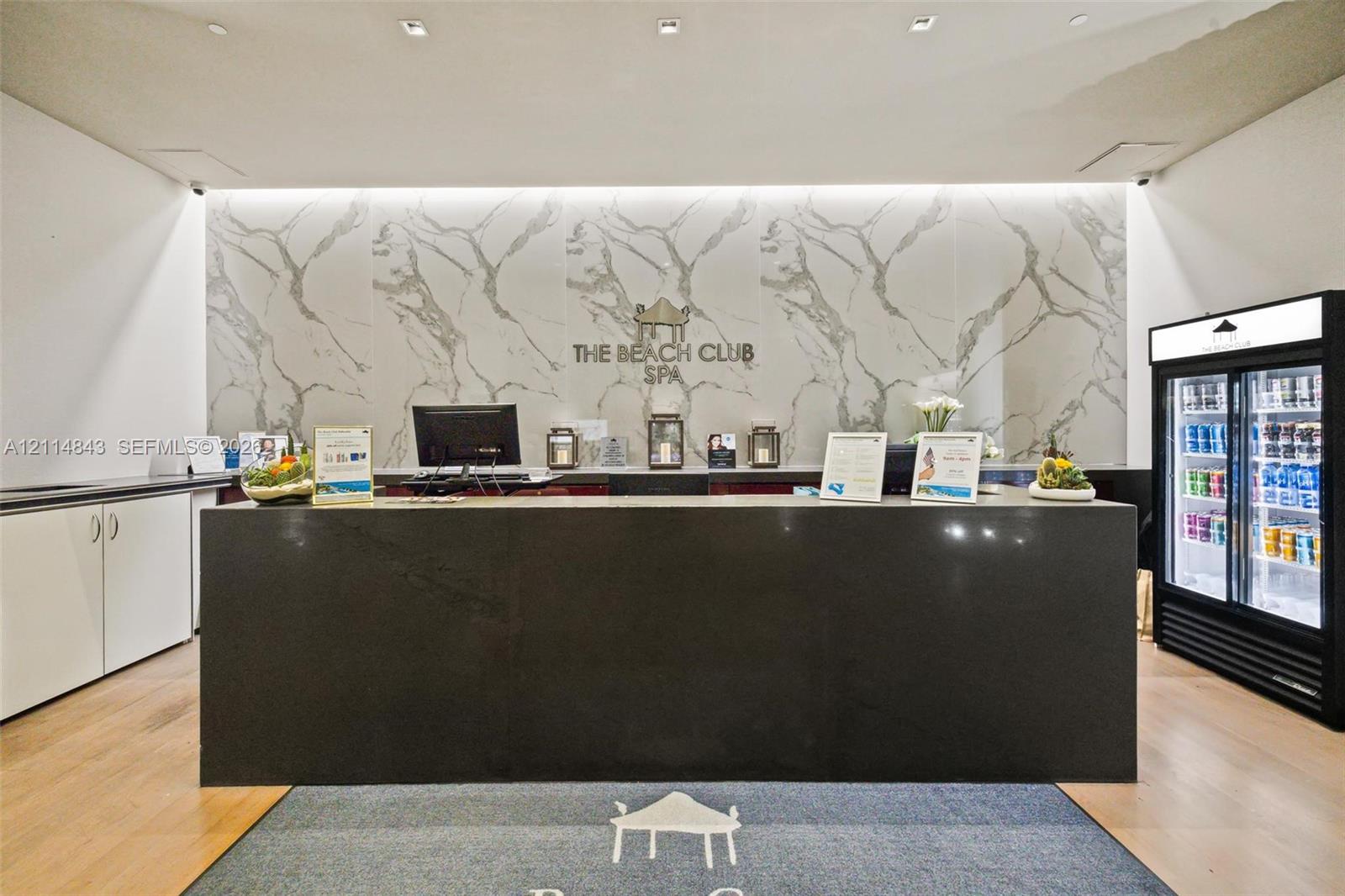Reception area featuring a dark stone-finish service counter, large-format veined accent wall, wood-finish flooring, and recessed ceiling lighting