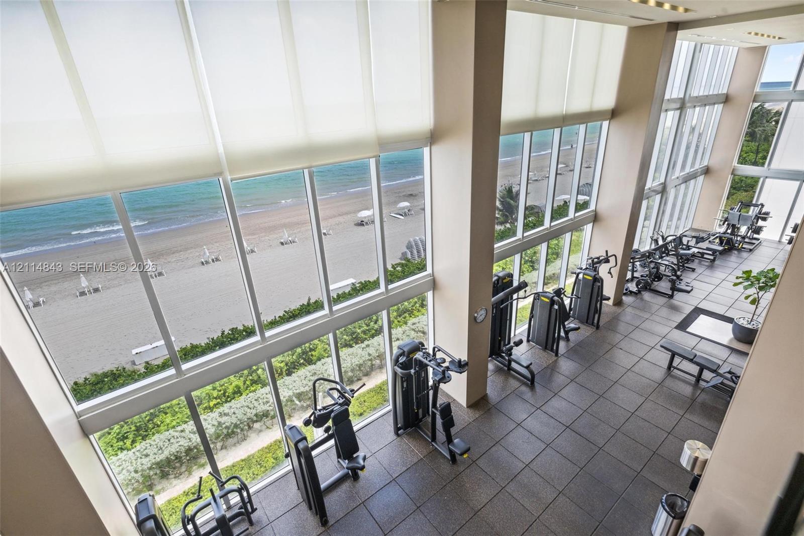 Fitness facility featuring double-height ceilings, floor-to-ceiling windows, ceramic tile flooring, and coastal scenery