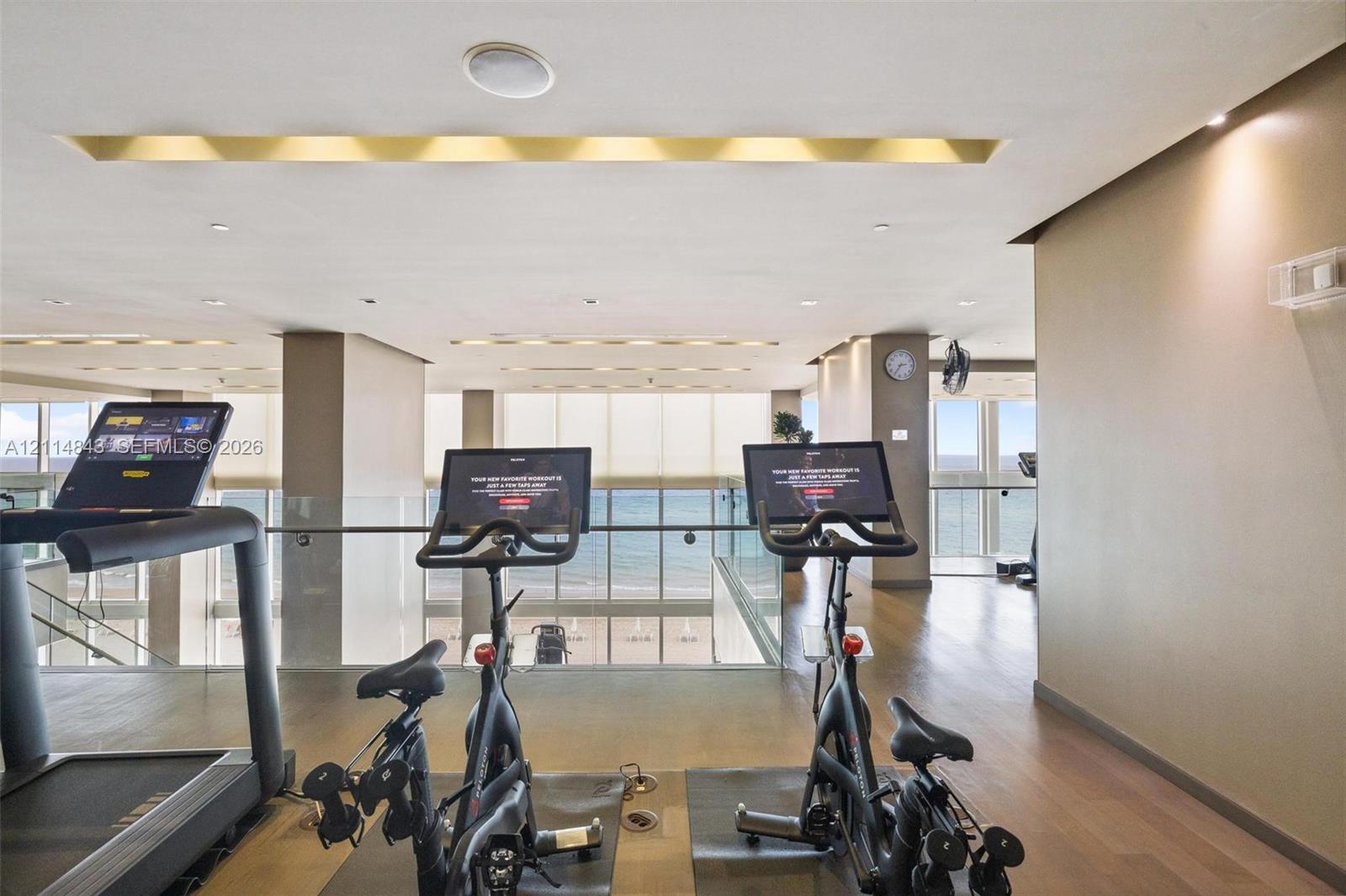 Fitness area featuring wood-finish flooring, recessed ceiling lighting, glass railings, and expansive windows with ocean scenery